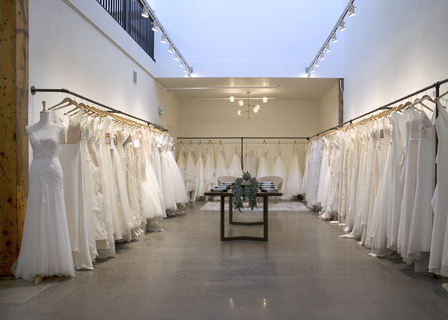 a view of the sales floor at Bespoke Bridal, dresses line the wall, a tuscan table-scape at the center, the elegance offset by concrete floors and exposed timber beams